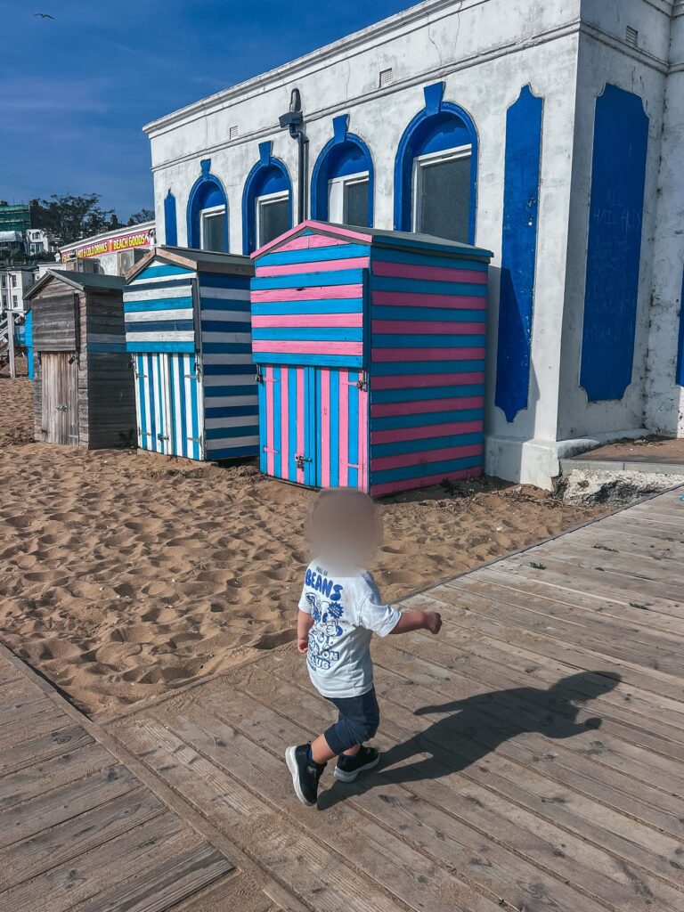 Toddler walking on the boardwalk past colourful striped beach huts at Broadstairs beach