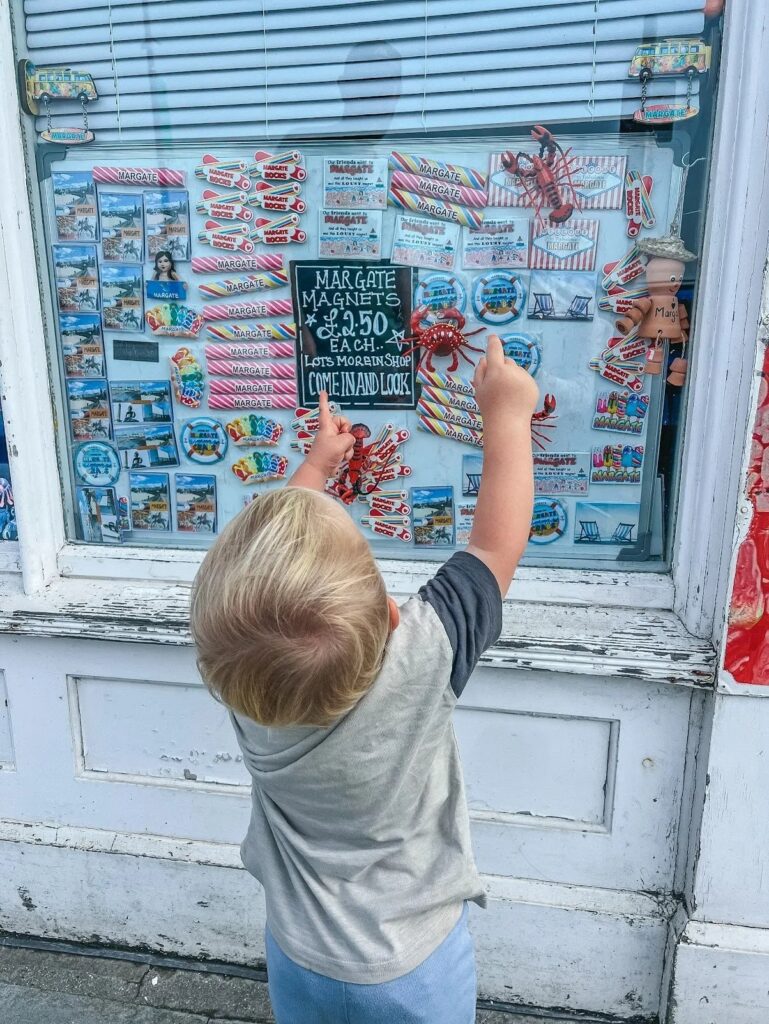 Toddler pointing at Margate fridge magnets and souvenirs in a seaside shop window