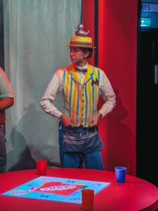 Monopoly Lifesized host in a striped waistcoat and straw boater hat standing at a table with a Monopoly board